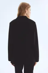 Blazer negro de corte entallado con solapas de muesca, cierre de un botón y hombreras. Presenta bolsillos delanteros ribeteados y abertura en la espalda.