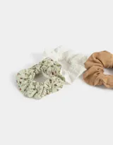 Set de tres scrunchies para el pelo con diferentes estampados: uno liso color marrón, uno blanco con bordado calado y uno con estampado floral en tonos verdes.