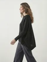 Poncho de tejido lurex color verde oliva con brillo sutil, de corte amplio y manga larga con puños acanalados. Presenta un bajo asimétrico con caída diagonal.