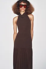 Vestido largo color marrón oscuro, con cuello halter que forma un drapeado en el busto. La parte superior es ajustada y la falda es larga con un panel inferior fruncido y drapeado en tela más liviana.