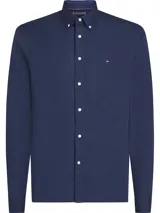 Camisa Tommy Hilfiger de corte slim fit, color azul marino, confeccionada en tejido dobby de algodón con tecnología Flex. Tiene cuello abotonado, manga larga y logo bordado en el pecho.