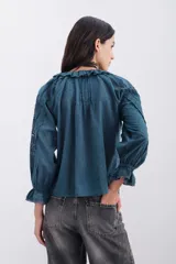 Camisa azul con botones al frente confeccionada en algodón, con detalles de plumetí, puntillas, alforzas y bordados. Mangas al codo abullonadas.