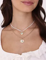 Collar corto doble de metal dorado, con una cadena de perlas y dije de corazón con flores esmaltadas, y otra cadena con dije redondo con flores esmaltadas.