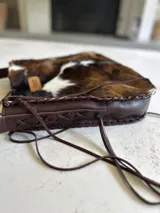 Bolso maxi de cuero con estampado de vaca en blanco y negro, y cuero color chocolate en la parte posterior. Tiene correa larga para colgar al hombro.