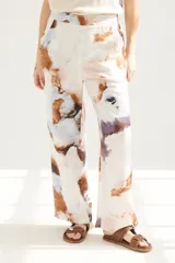 Pantalón de lino color blanco con estampado abstracto en tonos celeste, marrón y violeta.