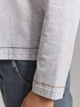 Remera gris claro de algodón con escote en V y bordados dorados y azul marino en los hombros.