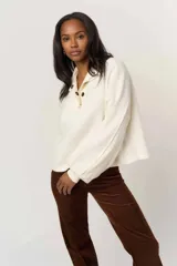 Buzo tipo henley de color blanco, confeccionado en tejido fleece suave. Presenta un diseño de calce fluido con hombros caídos, mangas oversized con puños y cuello con broches frontales destacados.