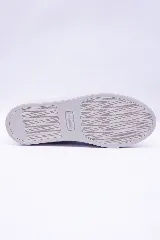 Zapatilla urbana de caña baja, color marrón cuero, con suela blanca gruesa. Presenta perforaciones a lo largo del cuerpo y cordones marrones. El logo de un pingüino se encuentra grabado en el lateral.