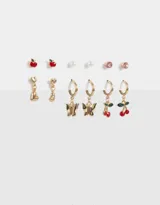 Set de seis pares de aros dorados con diferentes diseños: aros tipo botón con forma de manzana roja, perla, strass rosa; y aros colgantes con forma de corazón, mariposa y cereza.