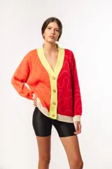Cárdigan tejido de punto con diseño abstracto en bloques de color rojo, naranja y amarillo. Tiene cuello en V, cierre con botones de madera y ribete en color crema.
