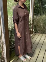 Vestido camisero largo color marrón chocolate, confeccionado en lino. Tiene cuello camisero, mangas 3/4 con trabilla y botón, cierre frontal con botones de nácar, corte a la cintura y abertura lateral en el ruedo.