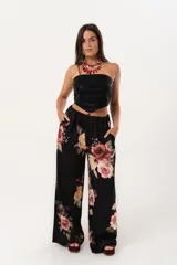 Pantalón palazzo negro con estampado floral en tonos rosa, naranja y amarillo. Tiene cintura alta con elástico.