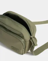 Bandolera negra de tela deportiva con bolsillo frontal con cierre, correa regulable y tag de goma.