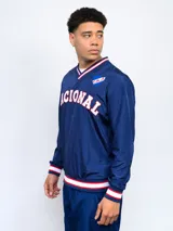 Buzo deportivo azul marino de nylon con cuello en V, puños y cintura acanalados con detalles tricolor (blanco, rojo y azul). Estampado frontal con la palabra "NACIONAL" en blanco y escudo del club C.N.de F. en el pecho. Corte clásico.