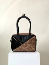 Cartera rígida negra de cuero con tachas plateadas y tres combinaciones de cuero diferentes que aportan textura. Tiene herrajes y cierre metálico plateado marca YKK. Cuenta con un asa fina para llevar al hombro o en la mano y una correa larga extra regulable.