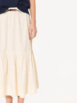 Pollera midi color verde grisáceo, confeccionada en poplín liviano. Presenta cintura elastizada con cordón ajustable, bolsillos tipo plaque con fuelle y tapa, y un recorte con volado fruncido en el ruedo.