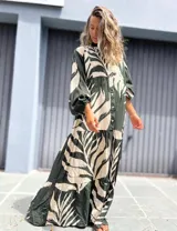 Vestido largo camisero de manga larga, con cuello mao y botones frontales. Presenta un estampado grande de hojas en color verde oscuro y crudo, con corte en capas en la falda.