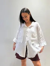 Camisa oversize rosada de lino, con cuello clásico, cierre frontal con botones, dos bolsillos de parche en el pecho y mangas largas con puños abotonados.