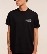 Remera negra de algodón con corte comfort, cuello redondo y mangas cortas. Estampa frontal con ángel y lettering en blanco.