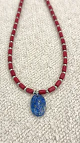 Collar corto con cuentas tubulares color borgoña y esferas plateadas, con dije ovalado de lapislázuli.