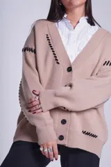 Cárdigan color beige con botones negros, escote en V y detalles de costuras bordadas en negro.