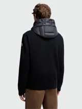 Campera Moncler con cuerpo acolchado negro, mangas largas de punto de lana negra y capucha con cordón ajustable. Cierre frontal con cremallera y bolsillos laterales con cremallera.