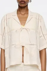 Camisa color crema de manga corta con cuello clásico y cierre frontal con lazos. Presenta bordados florales y calados.