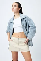 Minifalda color marrón claro, de corte recto con cierre metálico visible al frente y bolsillos decorativos con tachas.