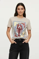 Remera color beige de algodón, de manga corta y cuello redondo. Estampado frontal con un dibujo de un sello con un langosta, un vaso de vino y limones.