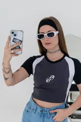 Remera corta gris con mangas raglán negras y logo bordado en el pecho.