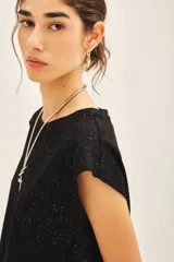 Remera negra de jersey con glitter, detalles en tela base en el frente y medallita marcaria en la espalda.