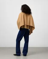 Chaqueta corta de color camel confeccionada en mezcla de lana y poliéster. Presenta cuello de solapa, manga larga de estilo japonés, cierre frontal con botones a tono y bolsillos laterales. Incluye un detalle de capa superpuesta en la espalda.