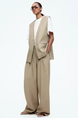 Pantalón color beige de corte ancho, con pinzas delanteras, cintura alta con elástico y bolsillos laterales.