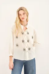 Camisa blanca de voilé de algodón con escote redondo y bordados de ojos en el delantero. De corte recto y mangas largas con puños abotonados.