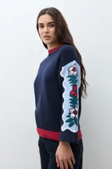 Sweater azul marino con cuello redondo y ribete rojo. Mangas anchas con diseño de jacquard floral en tonos celestes, rojos y verdes.