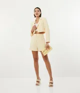 Blazer cropped color amarillo pastel, de crepé con forro de poliéster, cuello solapa, manga larga y cierre frontal con botón en forma de corazón.