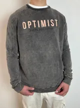 Buzo gris con efecto lavado y estampado con la palabra "OPTIMIST" en color salmón.