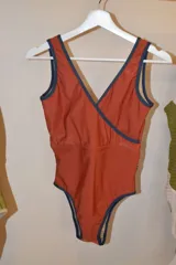 Traje de baño entero color terracota con escote cruzado y ribete azul marino.