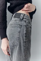 Jean tiro alto de denim negro rígido, lavado gris localizado con bigotes, pierna recta y apliques laterales de lentejuelas o tachas.