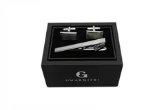 Set de gemelos y sujetacorbata plateados de la marca Guarnieri, presentados en caja negra con logo de la marca. Los gemelos son rectangulares con detalle de líneas horizontales y el sujetacorbata es liso.