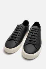 Zapatilla urbana de cuero sintético color negro, con cordones y suela de goma color crema.