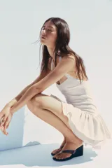 Minivestido blanco con cuello halter, escote recto y falda con volantes y forro tipo short. Presenta cierre con botones en el cuello y cremallera oculta en la espalda.