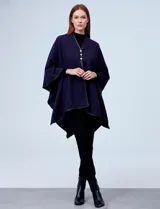 Ruana blanca de tejido suave, con ribete de eco cuero negro en los bordes y cierre frontal con botones metálicos dorados.