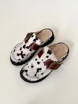 Zueco tipo mule negro, confeccionado en cuero vacuno, con puntera cuadrada y suela track gruesa. Presenta una faja ancha con hebilla metálica plateada sobre el empeine.