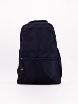 Mochila de tela color azul marino, con compartimento principal y bolsillo frontal con cierre. Presenta un asa superior y tirantes ajustables. En el lateral inferior izquierdo tiene una etiqueta negra con texto blanco.