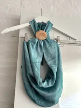 Top halter de color celeste/turquesa, con efecto drapeado y un accesorio tipo concha marina como broche central. El diseño es holgado y se ajusta en la espalda.