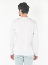 Remera blanca de algodón con cuello redondo y manga larga. Logo de Calvin Klein estampado en el pecho y diseño con letras en la manga.