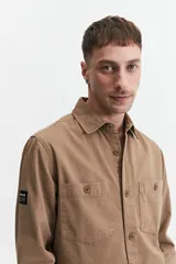 Sobrecamisa color marrón claro de twill de algodón, con cuello clásico, cierre frontal con botones a tono, dos bolsillos de parche con solapa abotonada en el pecho y mangas largas con puños abotonados.