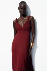 Vestido midi color borgoña con escote en V, tirantes anchos con detalle de nudo y falda plisada. Cierre trasero con cremallera oculta.
