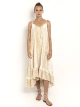 Vestido largo color crema con estampado dorado, de breteles finos y escote en V. Presenta una silueta amplia con caída fluida y detalle de volado en el ruedo.